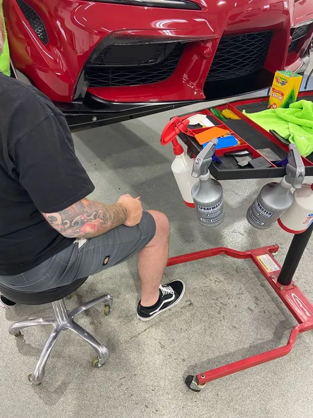 Installer trimming paint protection film on a red Supra bumper